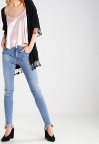 Musta kimono, jossa on hapsutettu helma, vaaleanpunainen satiininen toppi, vaaleansiniset pillifarkut raidoitetuilla resoreilla ja mustat korkokengät.