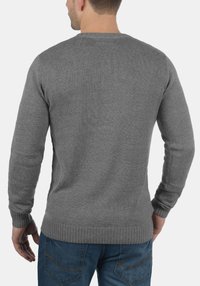 Maglione grigio a maglia con scollatura rotonda, polsini e orlo a costine, e una finitura testurizzata. Indossato con jeans blu, mostrando la vista posteriore.
