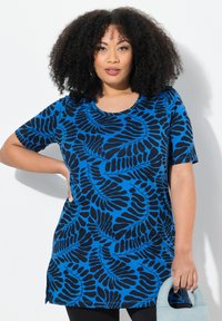 Túnica azul con patrón de hojas negras, mangas cortas, escote redondo y aberturas laterales, combinada con un bolso azul claro.