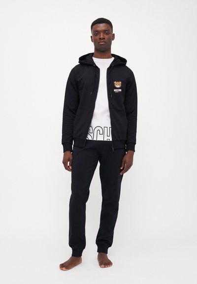 Black zip-up hoodie with a bear logo, white t-shirt with bold text, and black sweatpants. Cotton fabric, relaxed fit, minimal design.