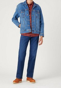 Jeansjack, lichtblauw, met twee borstzakken; geruit overhemd in rood en zwart daaronder; donkerblauwe jeans; bruine schoenen met witte zolen.