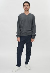 Grau-violetter Pullover mit V-Ausschnitt aus weichem Material, kombiniert mit marineblauen Hosen. Weiße Sneaker vervollständigen das Outfit. Minimalistisches Design, keine Muster.
