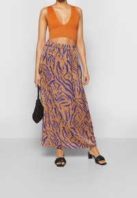 Oranžový žebrovaný crop top s hlubokým V-výstřihem, zkombinovaný s hnědou maxi sukni s fialovým tygřím pruhovaným vzorem. Černé robustní sandály a kabelka.