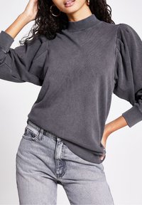 Grå tröja med hög krage och voluminösa puffärmar, i kombination med ljusgrå jeans som har en avslappnad passform och mjuk textur.