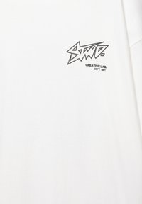 T-shirt bianco in cotone con un logo grafico nero caratterizzato da un testo angolare e la scritta "CREATIVE LAB." sottostante, posizionato nella parte sinistra del petto.