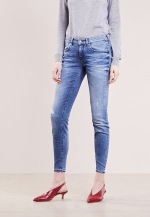 Wąskie niebieskie dżinsy w jasnym odcieniu z lekkim przecieraniem, noszone z szarą bluzką z długim rękawem oraz czerwonymi czółenkami na niskim obcasie z odkrytą piętą.