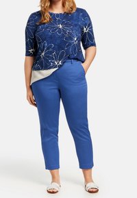 Námorníkový top s květinovým vzorem s bílými květinami, v kombinaci s modrými kalhotami na míru. Lehká tkanina a uvolněný střih, doplněný bílými sandály.