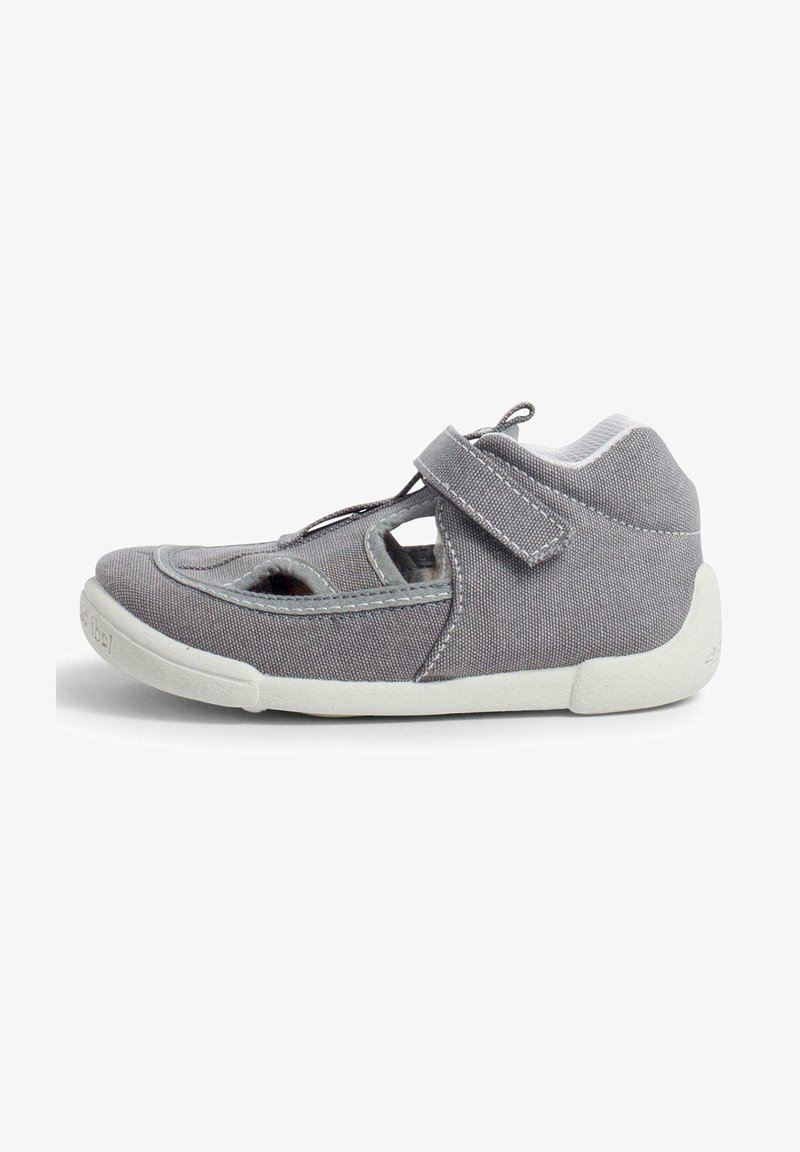 Chaussure en tissu gris avec des côtés découpés, une sangle à boucle velcro et une semelle en caoutchouc blanche ; présente un bout arrondi et un col rembourré pour le confort.