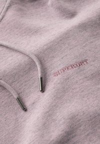 Różowy bawełniany sweatshirt z teksturowaną powierzchnią, sznurkami ze metalowymi końcówkami oraz haftowanym logo "SUPERDRY" w dopasowanym kolorze.