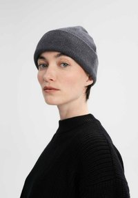 Grijze geribde gebreide beanie gedragen met kort haar, gecombineerd met een zwart gestructureerd sweater. Focus op het naadloze ontwerp van de hoed en het zachte materiaal.