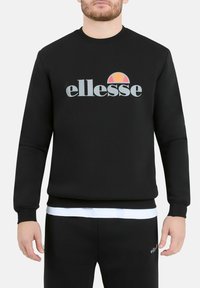 Felpa nera in misto cotone, con colletto a girocollo e polsini a coste. Presenta il logo "ellesse" e un design circolare colorato.