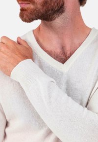 Leichter Pullover in Creme mit V-Ausschnitt. Verfügt über gerippte Bündchen und eine feine Strickstruktur, die ein mehrlagiges Stoffbild betont.