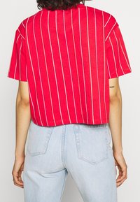 Punainen lyhyt t-paita, jossa valkoiset pystysuorat raidat, lyhyet hihat ja rento istuvuus. Vaaleansiniset farkut, joissa takataskut.