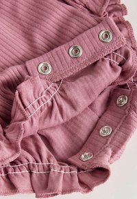 Roza rebrasta tkanina z nagubanim robom in kovinskimi zapiralčki na pritisni gumb. Tekstura je mehka, s kontrastnim belim šivom vzdolž šivov.