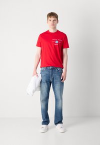Punane puuvillane T-särk "Calvin Klein" logoga ja sinine ristkülikukujuline aktsent, kombineerituna tuhmunud siniste teksade ja valgete tossudega.