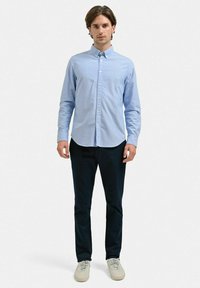 Ljust blå skjorta med knappar och klassisk krage, bärs med mörka byxor och beige sneakers. Skjortan har en mjuk textur och lång ärm.