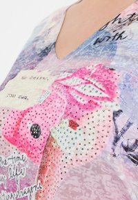 Top de manga corta con escote en V que presenta un diseño gráfico multicolor con texto, embellissements de strass y patrones texturizados variados.