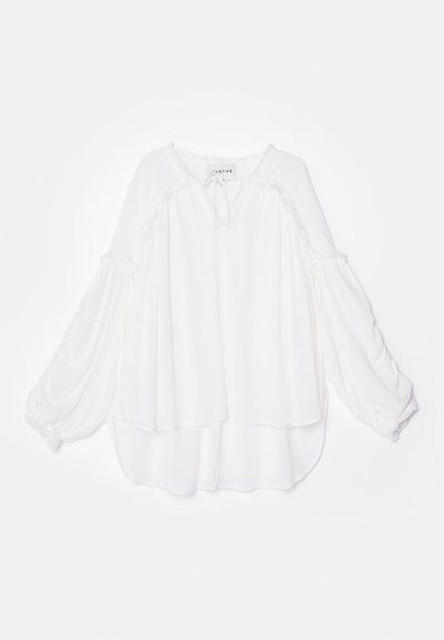 Valge pluus laia, kihilise disainiga. Omab pikki, hõljuvaid varrukaid ja tekstuurset ääret kaeluses ja allääres. Pehme kangas.