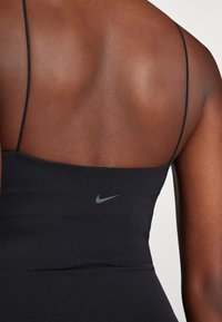 Melns sporta bez piedurknēm tops ar plānām siksnām, aizmugurē ar mazu pelēku Nike logotipu. Gluda tekstūra un pieguļošs dizains.