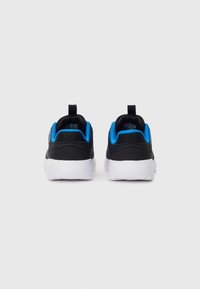 Et par sorte og blå sneakers med hvite såler sett fra baksiden på en ensfarget hvit bakgrunn.