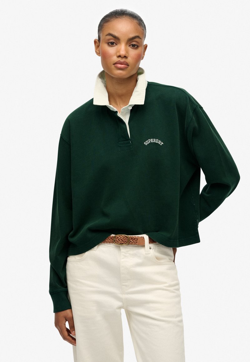 Ciemnozielona, długorękawowa koszulka polo z kremowym kołnierzykiem, posiadająca zapięcie z przodu i subtelny haft "Superdry". Połączona z kremowymi spodniami.