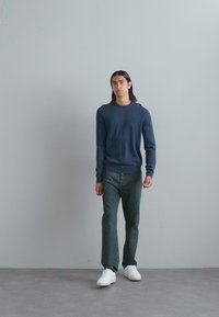 Navy crewneck sweater, dark gray straight-leg jeans, and white sneakers. Smooth texture with a relaxed fit, no visible patterns or accents.