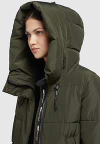 Giacca imbottita verde con un ampio cappuccio, chiusura con zip e tipi regolabili. Presenta un tessuto testurizzato e un tirazip con logo.