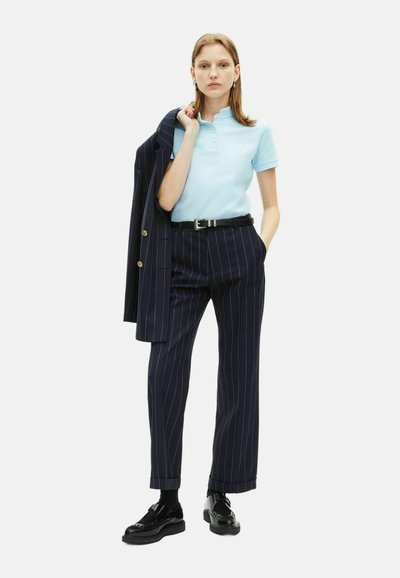 Polo shirt azzurro chiaro con colletto, abbinato a pantaloni blu navy a righe e a un blazer coordinato. Una cintura e scarpe nere completano il look.