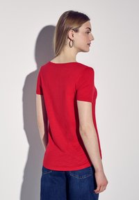 Rød kortærmet t-shirt med rund halsudskæring, lavet af glat stof. Stylet med blå jeans, der viser et enkelt og tætsiddende design.
