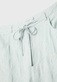 Pantalon vert menthe clair avec un motif texturé de feuilles, doté d'une taille nouée et de poches latérales. Confectionné dans un tissu doux et léger.