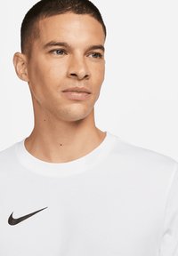Weißes T-Shirt mit kurzen Ärmeln und Rundhalsausschnitt aus Baumwolle, mit einem schwarzen Nike-Logo auf der oberen linken Seite. Glatte Textur, lässiges Design.