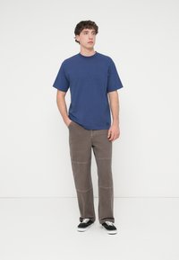 Μπλούζα από βαμβάκι σε ναυτικό μπλε με κοντά μανίκια, συνδυασμένη με καφέ παντελόνι κοτλέ με διακοσμητικές ραφές και μαύρα αθλητικά παπούτσια.