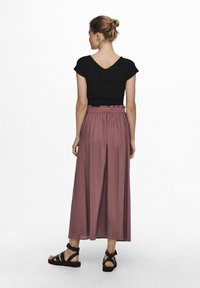 Zwarte top met korte mouwen en V-hals, gecombineerd met een roze, luchtige maxi-rok met een geplooide tailleband, en zwarte sandaaltjes met bandjes.