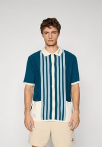 Kortermet skjorte i teal med vertikale striper i lyseblått og krem. Har en kontrasterende krage og lommer foran.