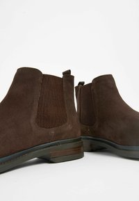 Botas de tobillo de ante marrón con paneles laterales elásticos, patrones texturizados y un tacón apilado. Presentan lengüetas en la parte posterior para facilitar su uso.