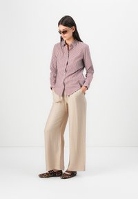 Collared, button-up shirt with red and white stripes, paired with beige wide-leg pants. Footwear features a leopard print design.
