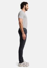 Heren grijze T-shirt, donker slim-fit jeans en witte sneakers. Opvallende details zijn de stoftextuur en stikselaccenten op de jeans.