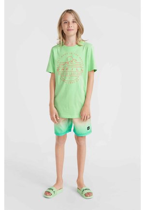 Grünes Baumwoll-T-Shirt mit aufgedrucktem Sonnen- und Wellenmotiv. Grüne Shorts mit Farbverlauf-Muster sowie passende grüne Schieber mit Logo.