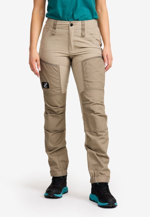 Beige trousers made of durable fabric featuring articulated knee panels, zip pockets, and elastic cuffs, paired with black and teal footwear.