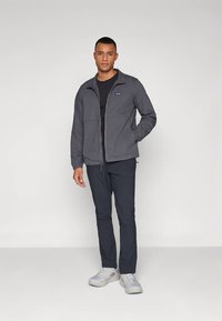 Gray zippered jacket with a stand-up collar, paired with a black shirt and navy pants. The individual wears light gray shoes.