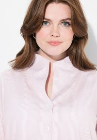 Camicia a righe rosa chiaro e bianco con scollatura alta, design con bottoni sul davanti e texture del tessuto morbida. Presenta un taglio senza colletto.