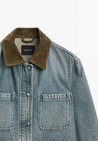 Denim jasje met een groene corduroy kraag, twee borstzakken en een vervaagde blauwe was. Label in de hals leest "Massimo Dutti."