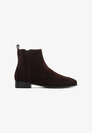 Stivale alla caviglia in suede marrone scuro con tacco basso, con linguetta sul retro e punta leggermente affusolata, mostrato di lato su uno sfondo bianco.