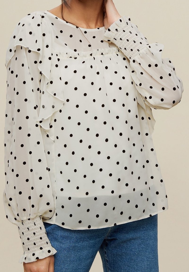 Weiße Bluse mit Punkten, Rüschendesign, transparenter Stoff und elastischen Manschetten. Merkmale sind ein runder Ausschnitt und ein leichter Stoff.