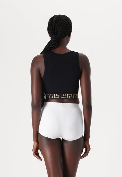 Black cropped tank top with a gold Greek key pattern at the hem, paired with white ribbed high-waisted shorts, viewed from the back.