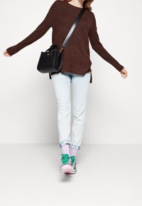 Hnědý texturovaný svetr, světle modré džíny, růžovo-zelené tenisky a malá černá kabelka přes rameno.