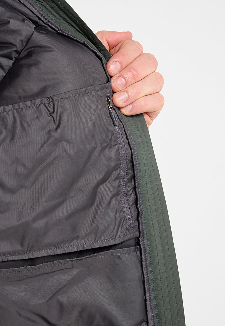 Interno della giacca verde con una fodera grigia, dotato di una tasca con zip e due tasche aggiuntive. Texture liscia e design trapuntato.