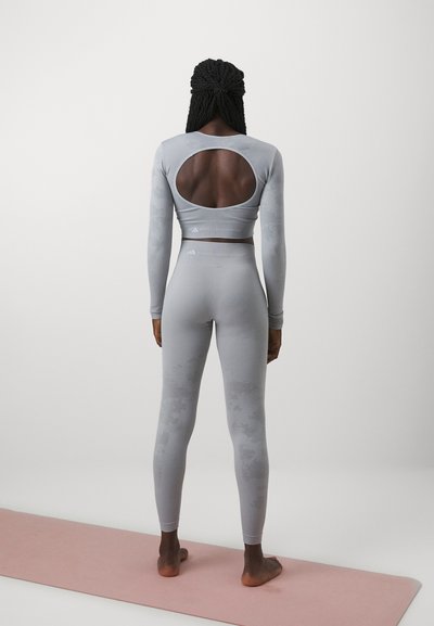 Tricou lung gri deschis, cu decupaj circular în spate și colanți înalți asortați, având un model texturat subtil.