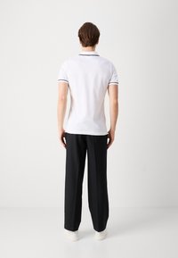 Vit polo skjorta med svarta accenter, kombinerad med svarta byxor och vita sneakers. Skjortan har en klassisk krage och korta ärmar.