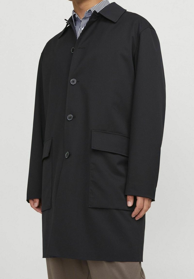 Black waterproof trench coat with a standard collar, front buttons, side pockets, and a straight cut. Made from smooth, durable fabric.